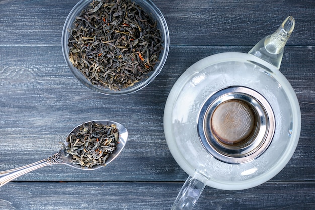 Vista superior una tetera de agua caliente y un tazón con una hoja de té en el escritorio de madera gris. Beber para relajarse.