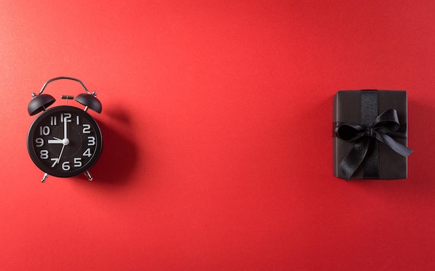 Vista superior del texto de venta de viernes negro con reloj despertador y caja de regalo sobre fondo rojo. Concepto de compras Boxing Day y composición del Black Friday.