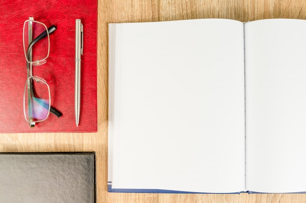 Vista superior de tiro de diario cuaderno en blanco vacío y gafas con libro de tapa dura en la mesa de madera