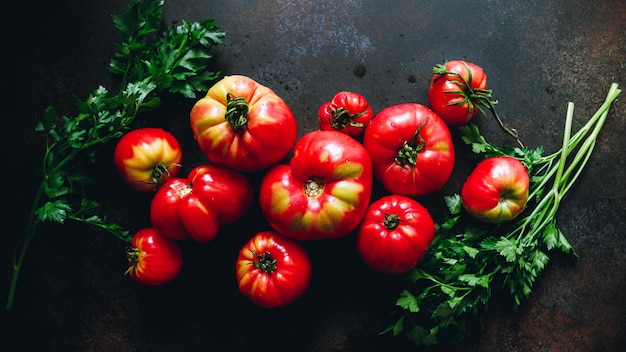 Vista superior de tomates maduros con verduras frescas sobre un fondo oscuro
