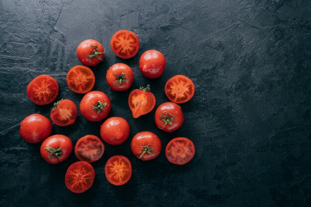 Vista superior de tomates muy maduros y rodajas sobre fondo oscuro con espacio libre.