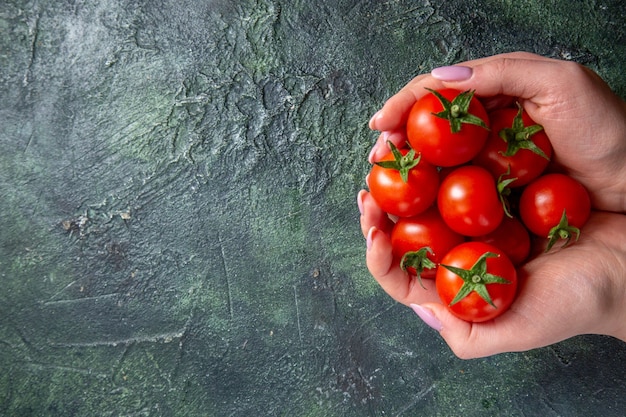 Vista superior de tomates rojos frescos en manos femeninas sobre superficie oscura