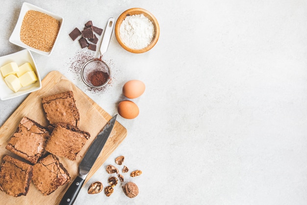 Vista superior de la torta de brownie casera recién horneada dispuesta con ingredientes de la receta en blanco rústico.