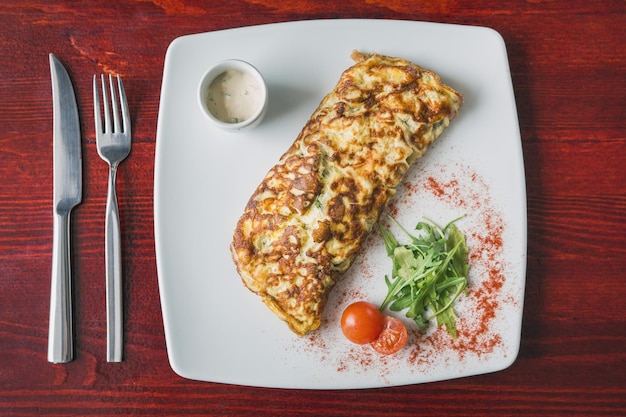 Vista superior de la tortilla con tomate cherry y verduras en un plato blanco, fondo de alimentos, cerrar