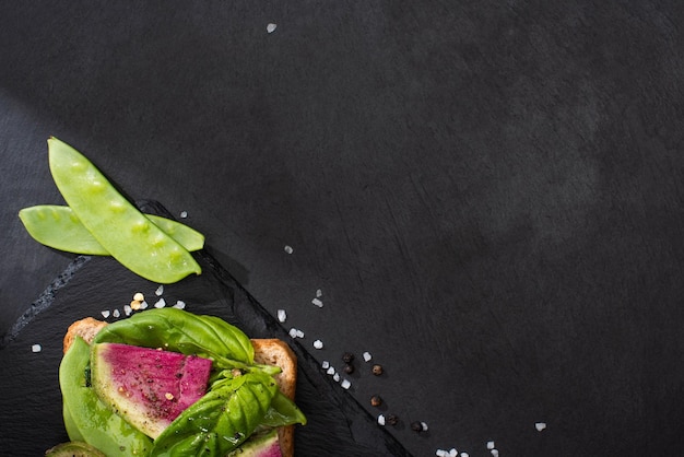 Vista superior de tostadas de rábano en tabla de cortar de piedra con semillas de pimienta y sal