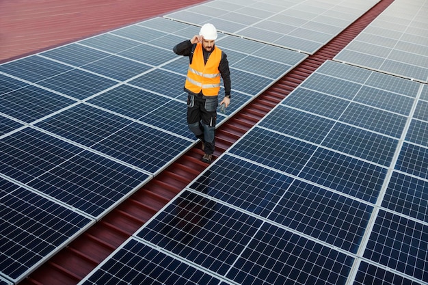 Foto vista superior del trabajador caminando entre paneles solares y comprobándolo