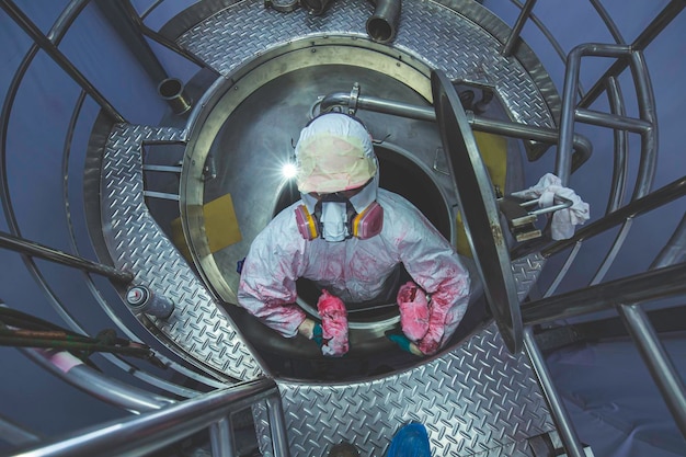 Vista superior del trabajador masculino suba las escaleras hacia el espacio confinado del área química inoxidable del tanque