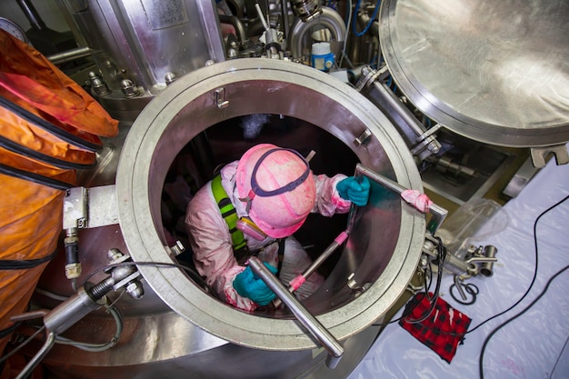 Vista superior trabajador masculino subir las escaleras hacia el tanque de acero inoxidable área química espacio confinado ventilador de seguridad aire fresco