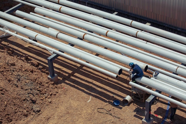 Vista superior trabajador masculino tubos largos de acero y codo de tubería tanque de aceite de nueva construcción de tubería de soldadura industria de petróleo y gas