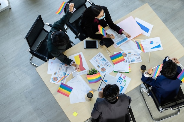 Vista superior Trabajadores exitosos Grupo de socios comerciales asiáticos con máscara protectora casual con diversos géneros (LGBT) juntando sus manos en una reunión en la sala de la oficina, COVID-19