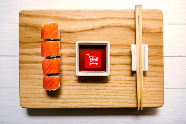 Vista superior del tradicional rollo japonés con salmón, con un botón de pedido dibujado, en forma de cesta del supermercado. comprar sushi en línea