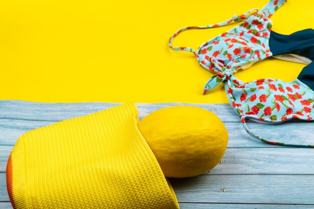 Vista superior de un traje de baño y un melón en una bolsa, acostado sobre un fondo de madera azul y amarillo.Concepto de vacaciones de verano