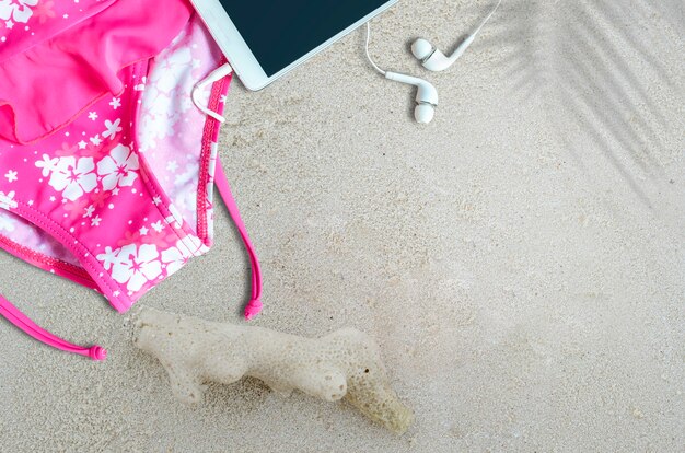 Vista superior de traje de baño rosa y teléfono inteligente en la playa de arena.