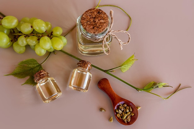 Vista superior de tres botellas de aceite de semilla de uva natural y una cuchara de madera con semillas sobre un fondo beige con una vid