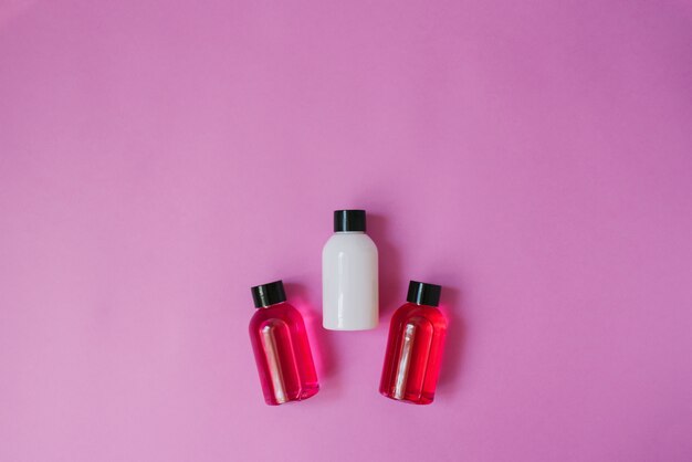 Foto vista superior de tres botellas pequeñas de blanco y carmesí y productos para el cuidado del cuerpo y el cabello sobre un fondo rosa. cosmeticos para turistas