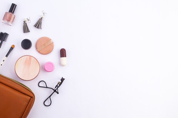 Vista superior Um conjunto de kits de maquiagem feminina está fora de uma bolsa de maquiagem marrom em um fundo branco