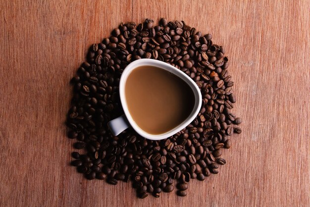 Vista superior Uma xícara de café cappuccino cercada por grãos de café no meio de uma mesa de madeira