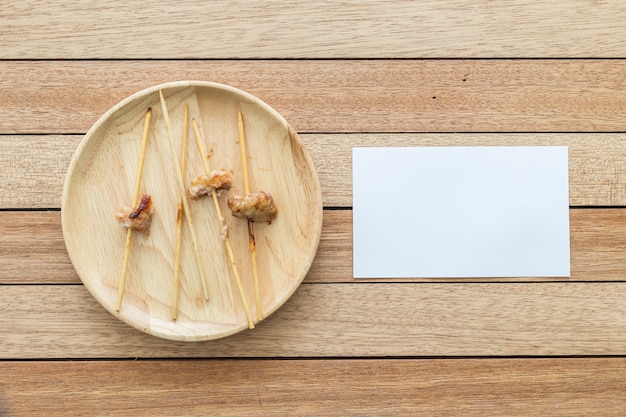 Vista superior vara de bambú vacía de cerdo a la parrilla y nota de papel sobre plato de madera