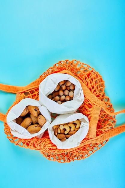 Vista superior de varios tipos de frutos secos sobre la mesa en una bolsa de papel en la bolsa de la compra sobre fondo azul, Cero desperdicio de alimentos. Vida libre de desperdicios, entrega de nueces. Copie el espacio.