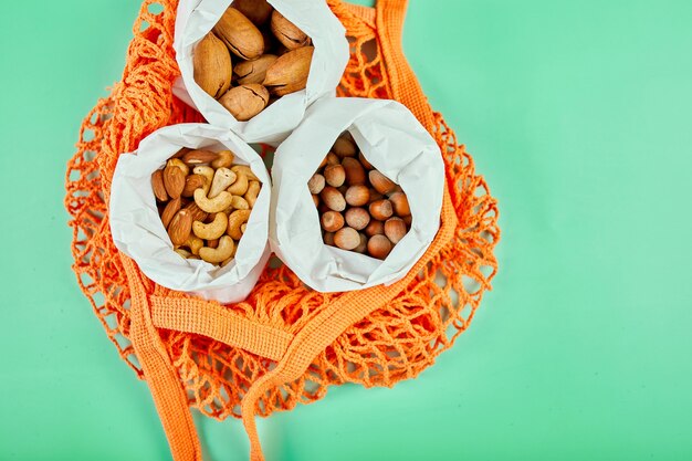 Vista superior de varios tipos de nueces sobre la mesa en una bolsa de papel en la bolsa de la compra en superficie verde