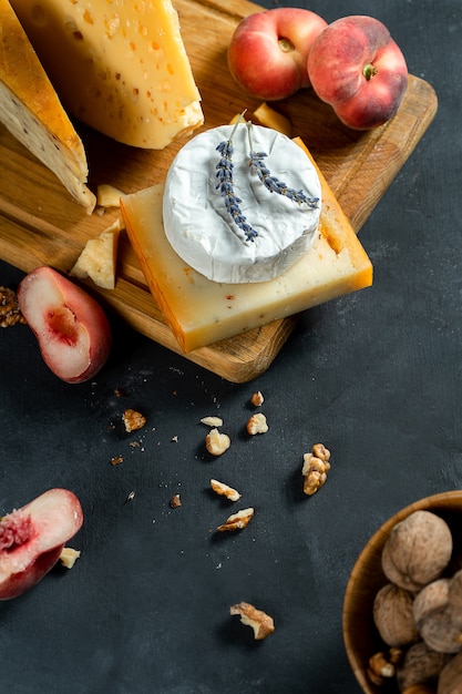 Vista superior de varios tipos de queso sobre fondo oscuro. Camembert, queso con especias, queso holandés en tabla de cortar con nueces, lavanda y durazno. Copia espacio Plana pone comida. Enfoque selectivo y suave