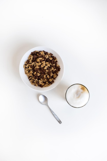 Vista superior del vaso de café con leche y copos de maíz en un tazón con una cuchara aislada en blanco