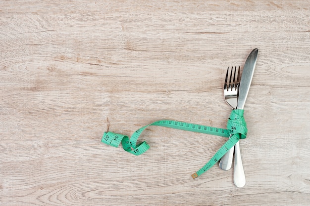 Vista superior Verde fita métrica enrolada em garfo e faca no fundo da mesa de madeira. conceito de dieta, perda de peso, obesidade e controle de alimentos