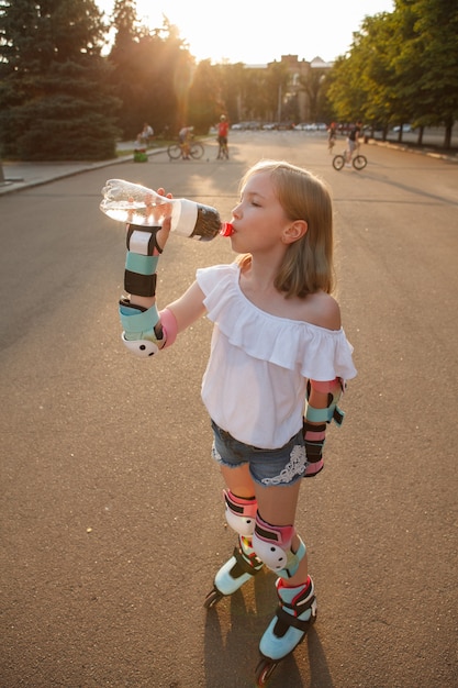 Vista superior vertical de una niña bebiendo agua, descansando después de patinar al aire libre