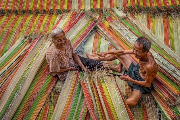 Vista superior del viejo artesano amante vietnamita haciendo las esteras tradicionales de Vietnam con acción de felicidad