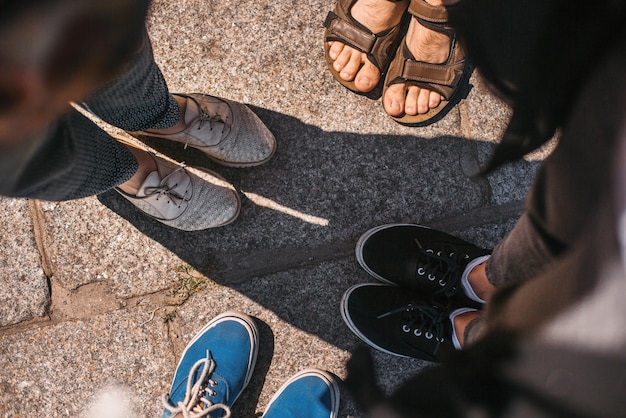 Vista superior de los zapatos de los amigos en las piernas de la carretera de un grupo de personas en la calle de la ciudad en las vacaciones de verano de un día soleado