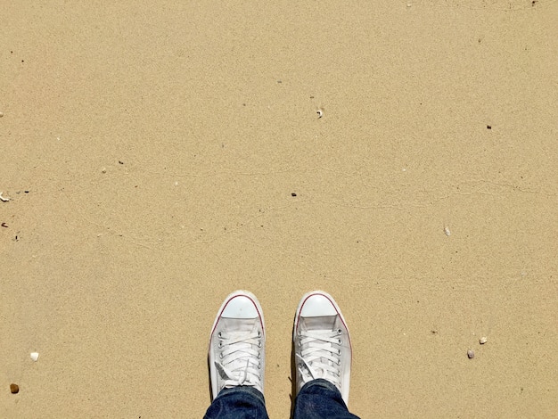 Vista superior de zapatos blancos sobre fondo de textura de playa de arena