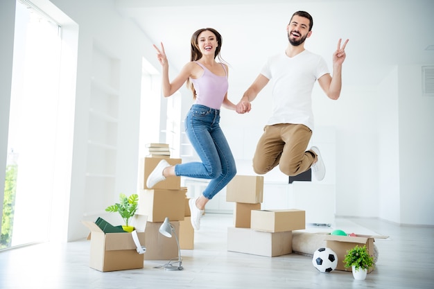 Vista del tamaño del cuerpo de longitud completa de agradable atractivo encantador alegre alegre alegre alegre pareja afortunada saltando divirtiéndose mostrando seguro de propiedad de seguridad de préstamo con signo v en el apartamento de la casa interior blanco claro