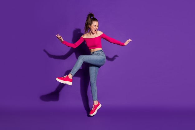 Vista del tamaño del cuerpo de longitud completa de la atractiva chica alegre y feliz divirtiéndose saltando bailando aislado sobre fondo de color violeta brillante