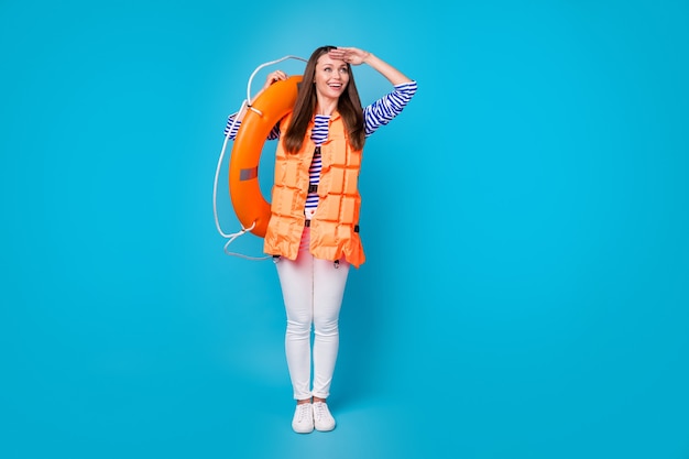 Vista del tamaño del cuerpo de longitud completa de ella, atractiva chica alegre de ensueño bastante curiosa con chaleco flotador con boya salvavidas, mirada lejana, aislado, brillante, vivo, vibrante, color azul, fondo