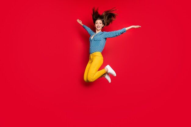 Vista del tamaño del cuerpo de longitud completa de la encantadora niña alegre alegre descuidada saltando divirtiéndose aislado sobre fondo de color rojo brillante