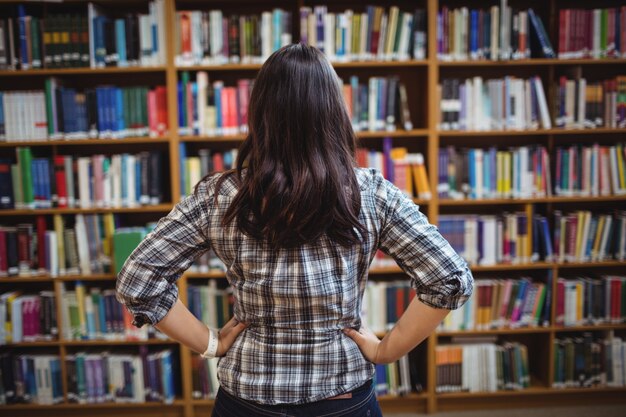 Vista traseira da aluna olhando livros na prateleira