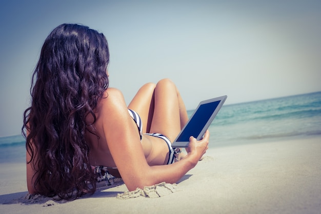 Vista traseira da bela morena com tablet pc na praia