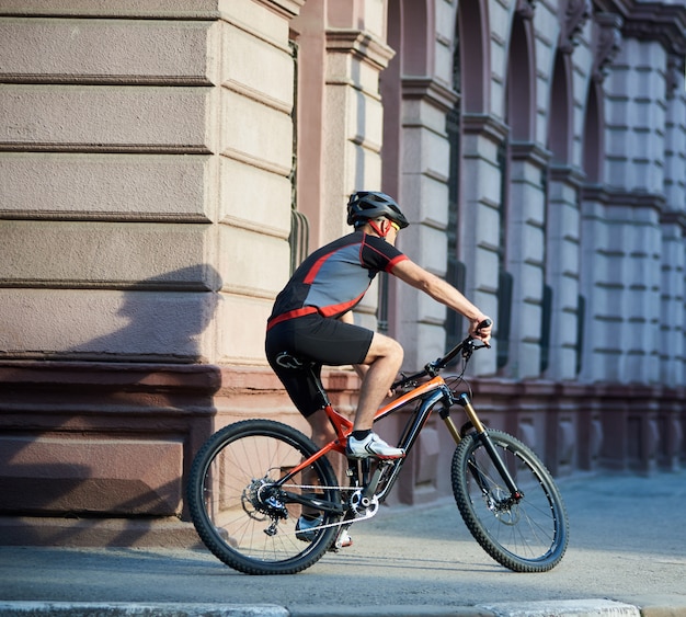 Vista traseira da bicicleta de equitação ciclista atlética no centro da cidade, correndo e passando de edifícios. Desportista de treinamento, exercício ao ar livre. Conceito de estilo de vida saudável