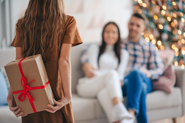 Vista traseira da criança segurando uma caixa de presente perto da árvore de Natal dentro de casa