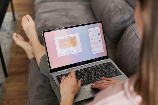 Vista traseira da jovem descansando no sofá com laptop, ela assistindo vídeo online ou fazendo trabalho online