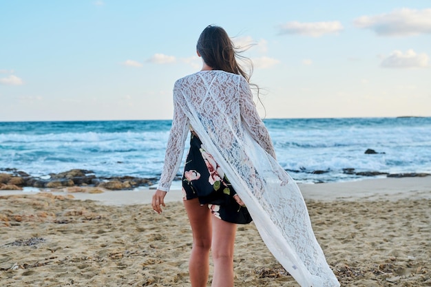 Vista traseira da jovem em roupas românticas da moda andando na praia