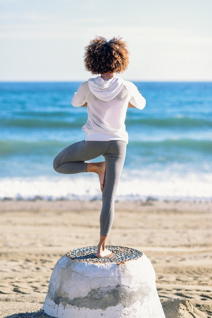 Foto vista traseira da jovem mulher negra fazendo yoga na praia