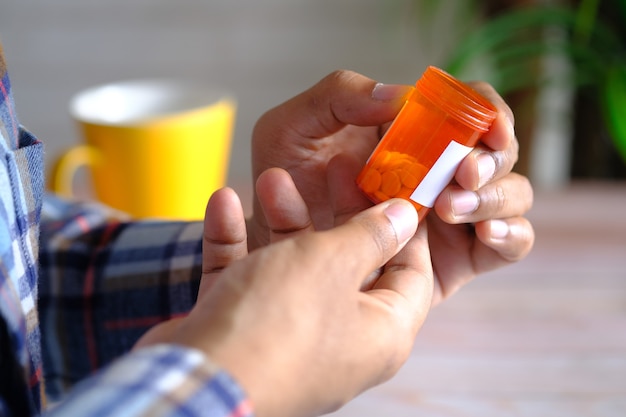Vista traseira da mão do jovem segurando um recipiente de pílulas médicas