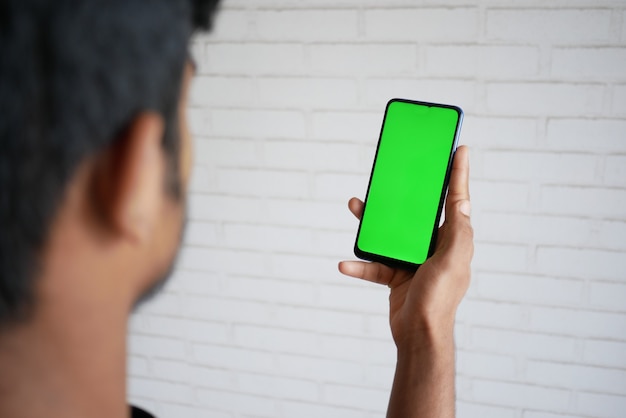 Vista traseira da mão do jovem usando telefone inteligente com tela verde