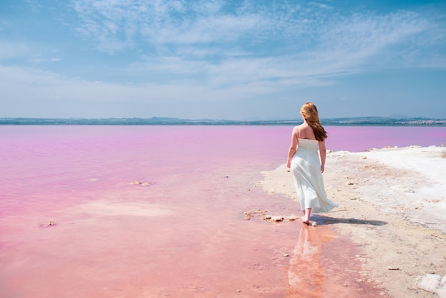 Vista traseira da mulher adolescente bonito vestido branco andando em um lago rosa incrível