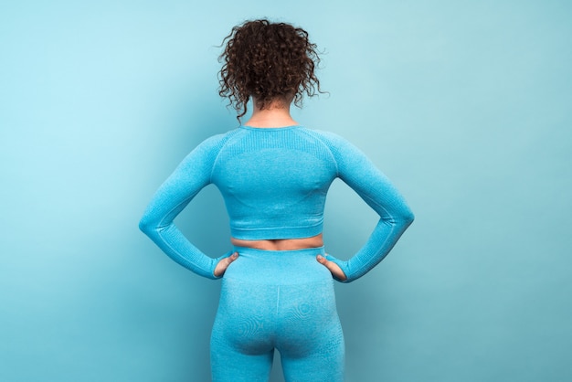 Vista traseira da mulher adulta caucasiana de aptidão em pé após o exercício isolado em um fundo azul com espaço de cópia. Conceito de treino de menina saudável