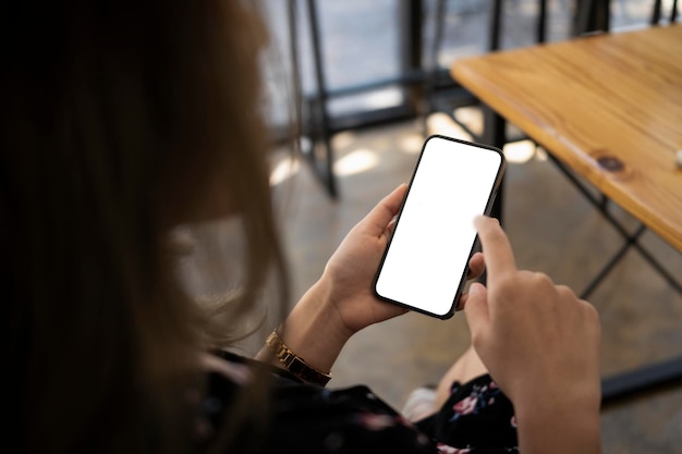 Vista traseira da mulher asiática sentada na xícara de café e usando telefone inteligente