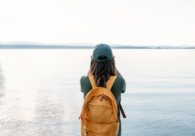 Vista traseira da mulher com mochila amarela olhando através de binóculos para pássaros no lago Birdwatching