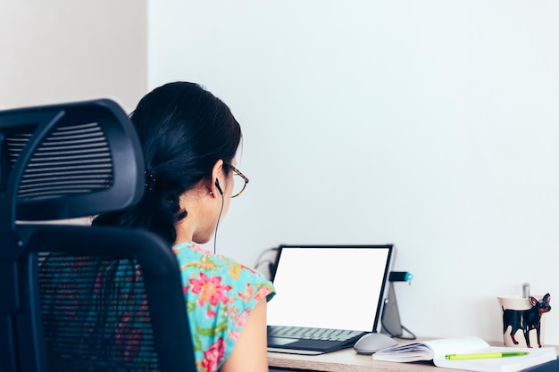 Vista traseira da mulher em fones de ouvido fazendo videochamada no laptop.