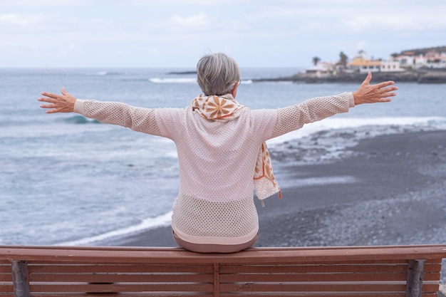 Vista traseira da mulher idosa sentada em um banco de frente para o mar olhando para o horizonte sobre a água Mulher idosa caucasiana ativa desfrutando de liberdade e férias